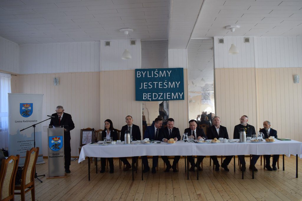 Mężczyzna przemawia przy mównicy. grupa osób siedzi za stołem.