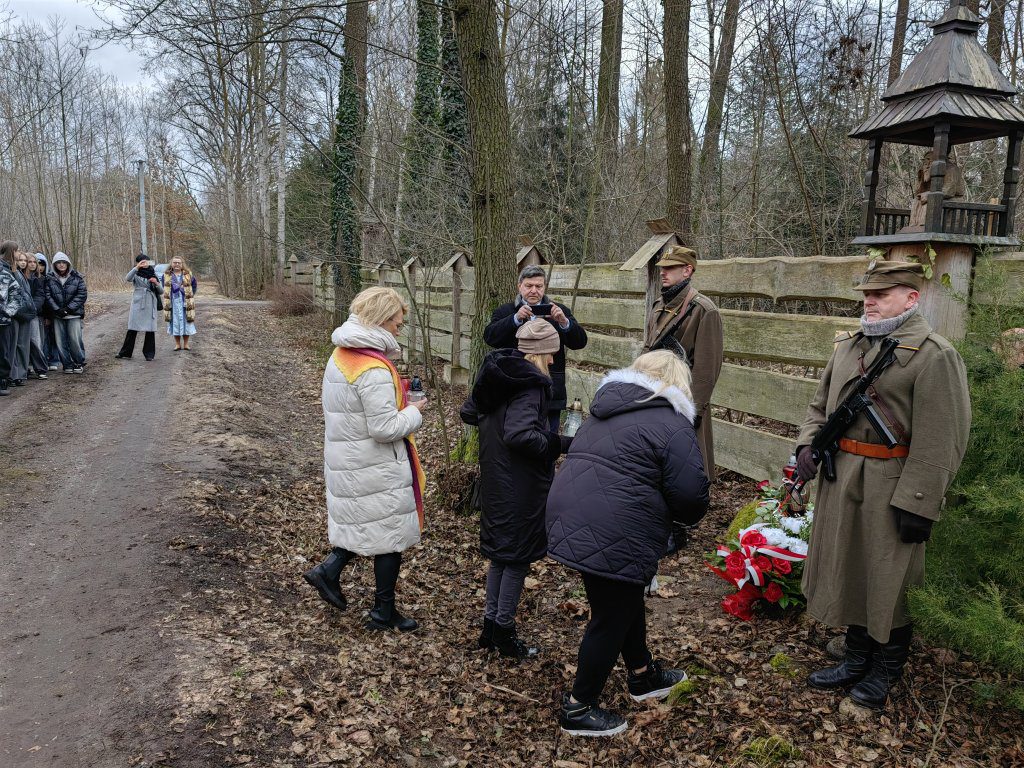 Osoby składają kwiaty i zapalają znicze