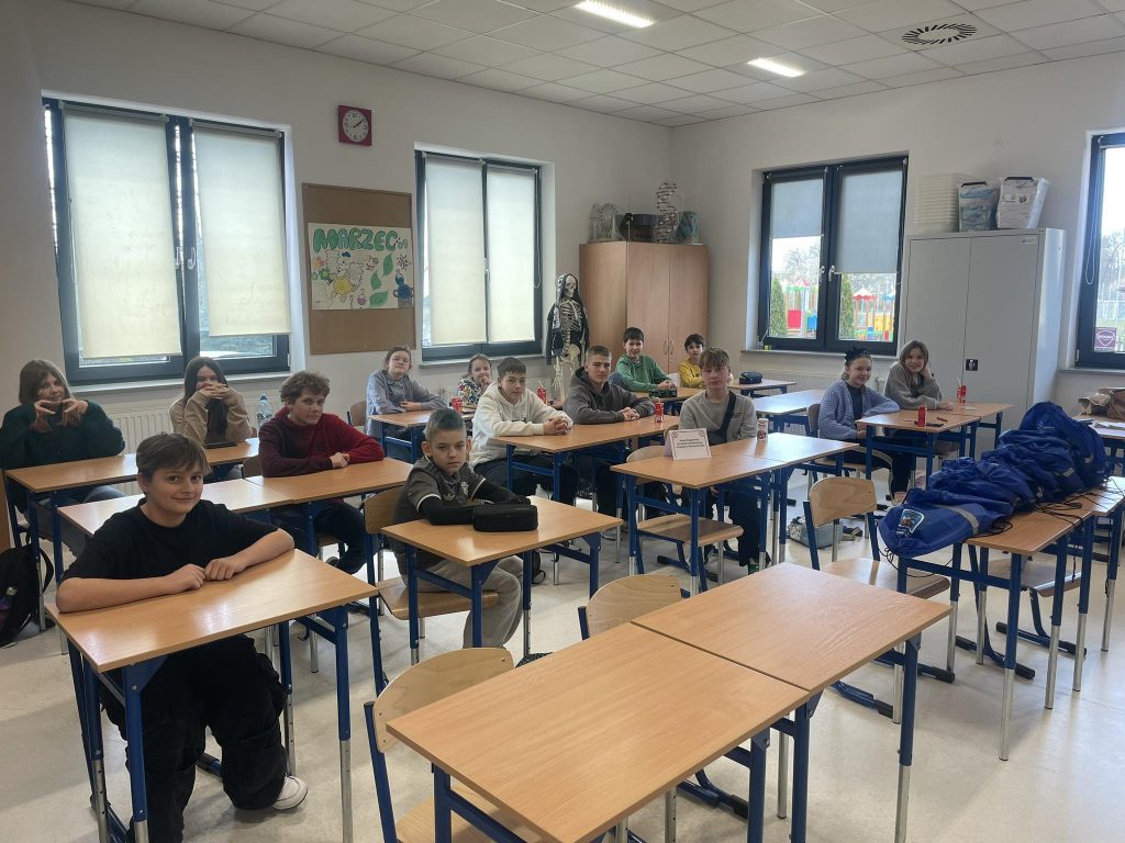 Dzieci siedzą w ławkach i piszą