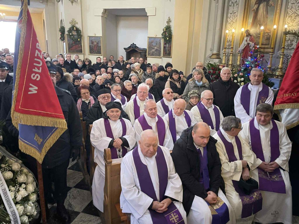 Grupa duchownych w fioletowych stułach siedząca w ławkach kościelnych
