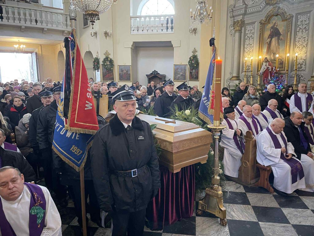 Widok na trumnę, poczty sztandarowe i zgromadzonych żałobników w nawie