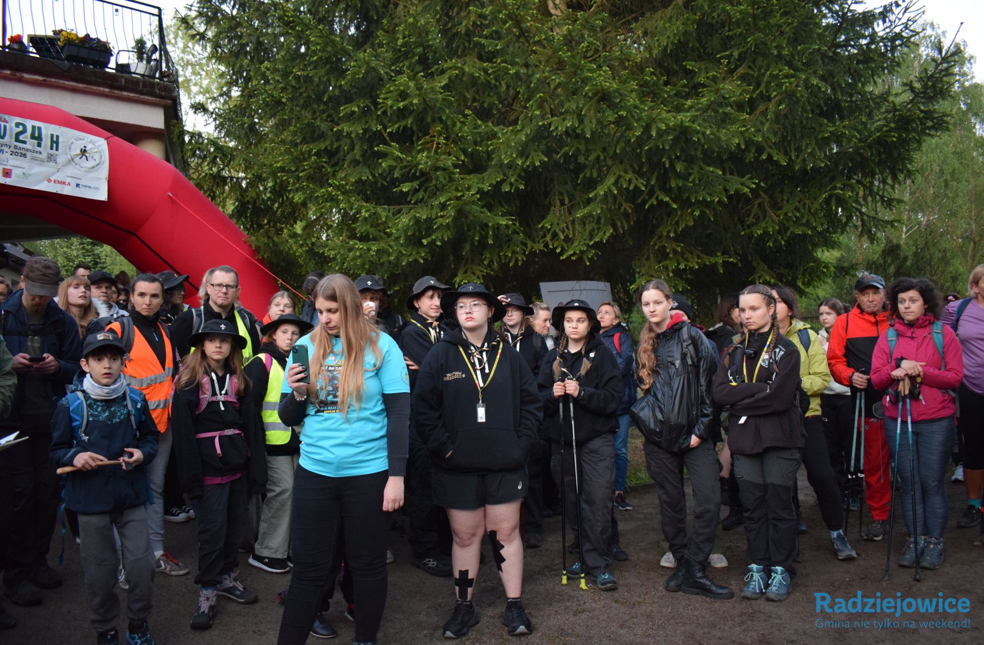 Harcerze i uczestnicy zgromadzeni przy miejscu startu Marszu 100 km w 24 h. W tle widoczny czerwony łuk startowy