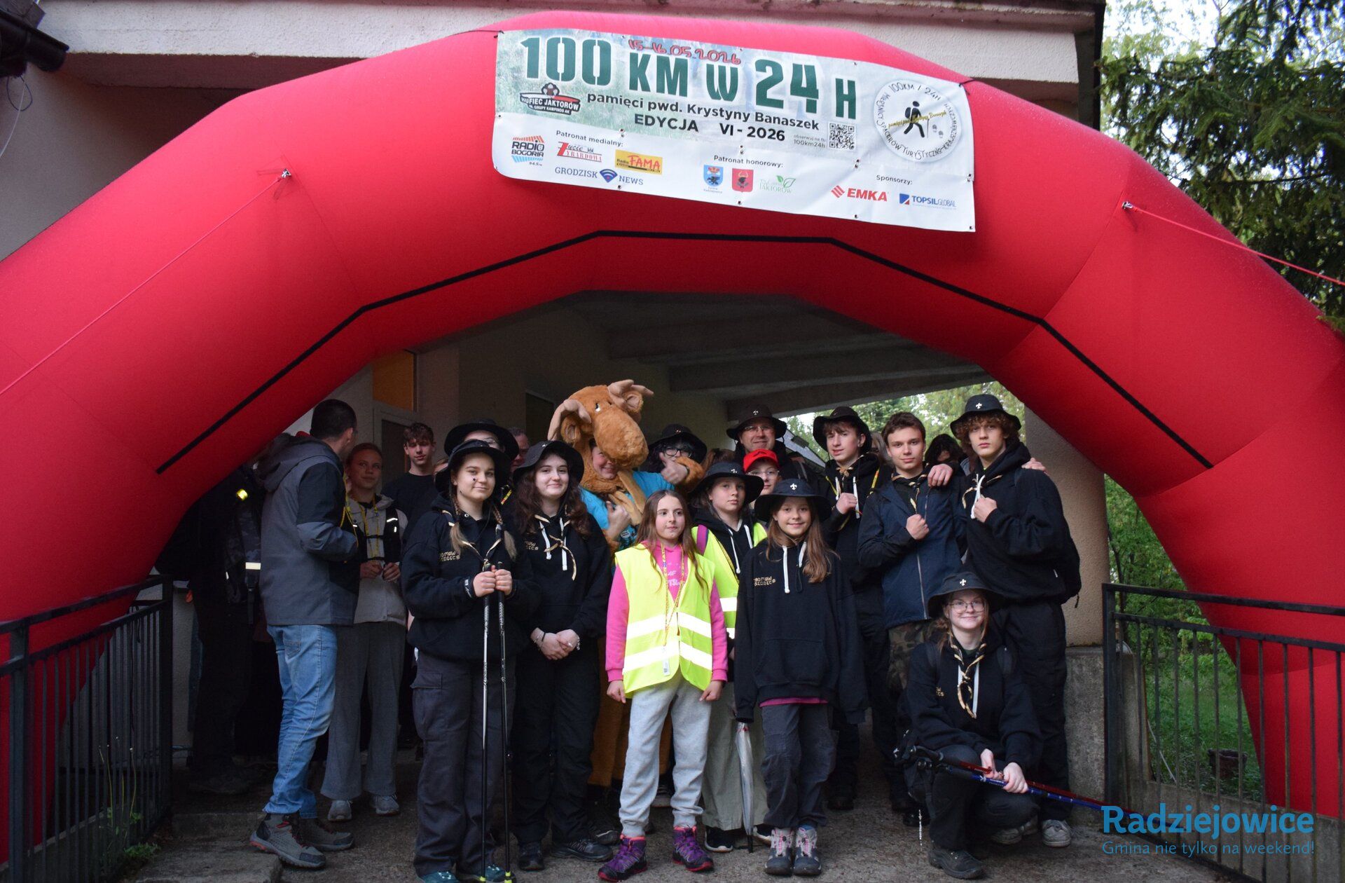 Harcerze oraz dzieci pozują do wspólnego zdjęcia pod łukiem startowym Marszu 100 km w 24 h