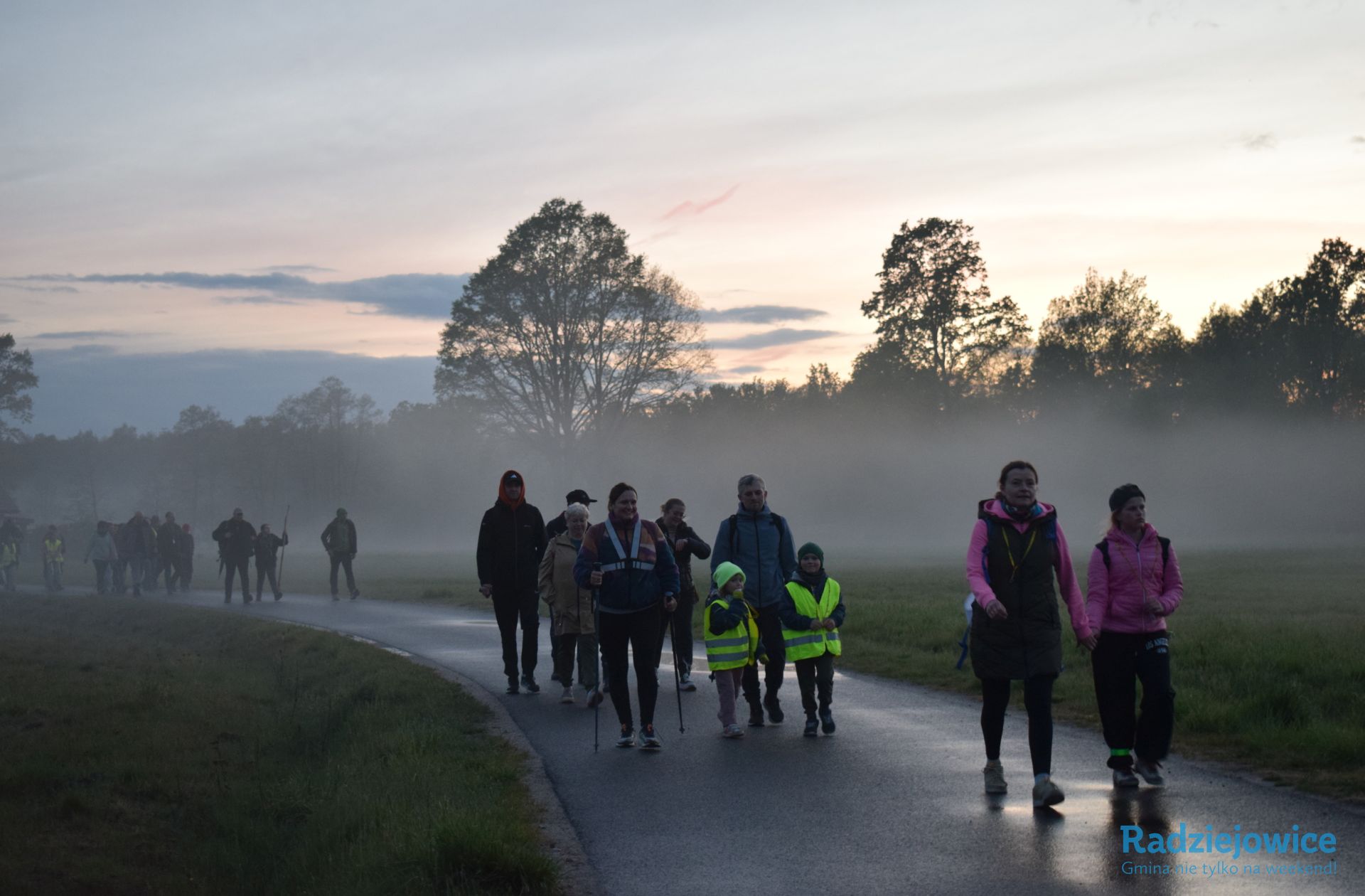 Uczestnicy Marszu 100 km w 24 h idą drogą wśród pól podczas wieczornej mgły. W grupie znajdują się osoby dorosłe i dzieci