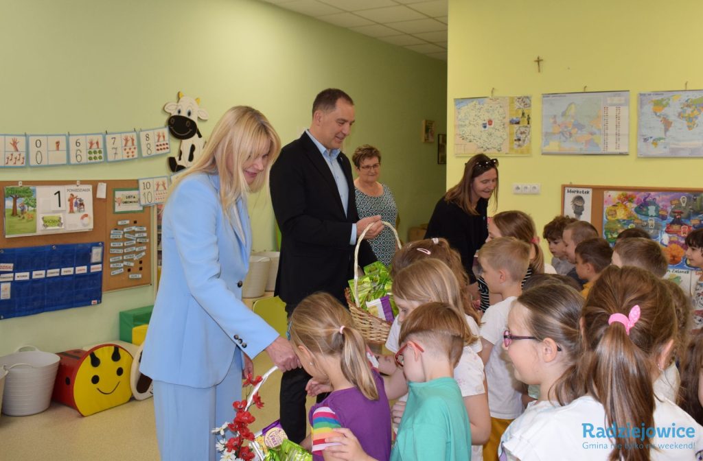 Przedstawiciele gminy wręczają dzieciom upominki w przedszkolu. Dzieci podchodzą kolejno do koszy przygotowanych z okazji święta.