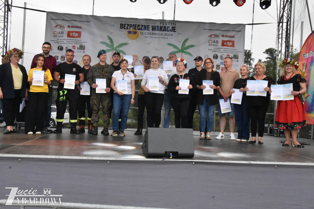 Uczestnicy i przedstawiciele różnych instytucji stoją na scenie, prezentując dyplomy otrzymane podczas wydarzenia.
