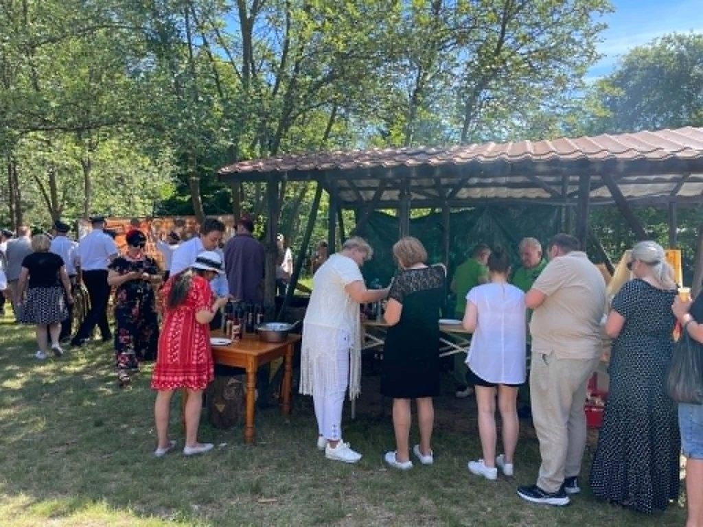 Uczestnicy ustawiają się w kolejce do wydawania posiłków przy zadaszonej wiacie z grillem.