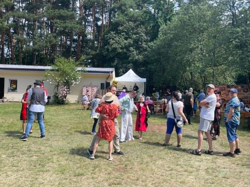 Uczestnicy wydarzenia tańczą na trawniku przed sceną podczas plenerowego spotkania.