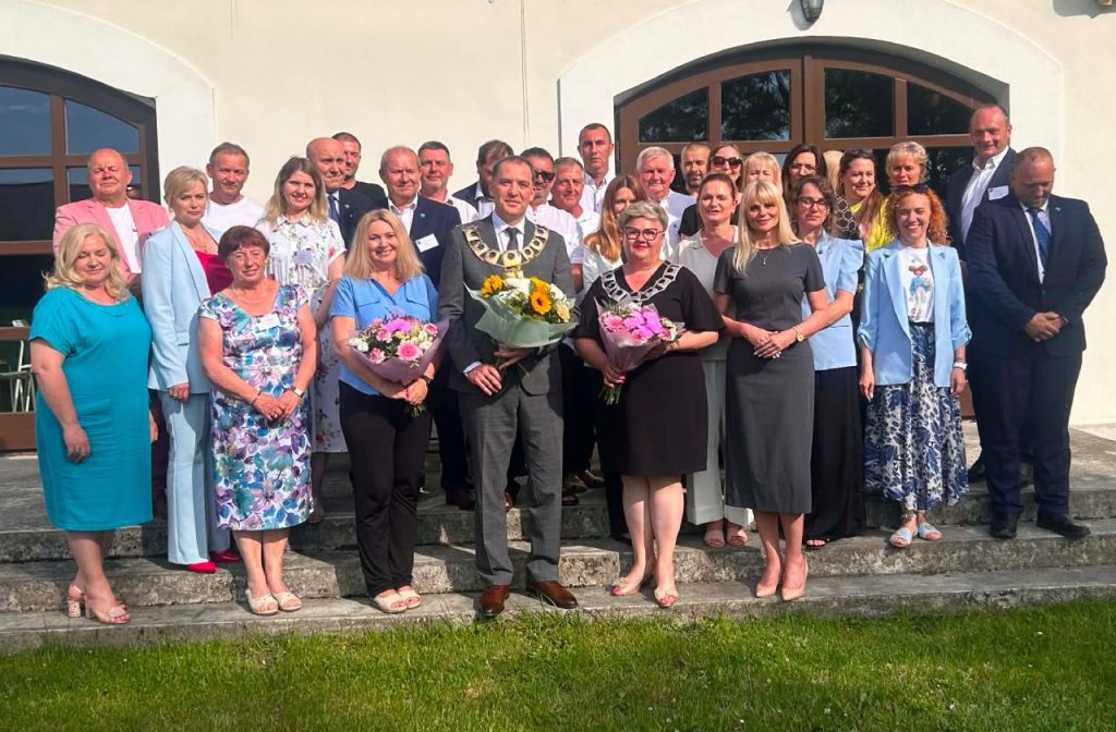 grupa wszystkich obecnych na sesji pozuje do zdjęcia. Wójta, Przewodnicząca Rady i Skarbnik Gminy trzymają w rękach bukiety kwiatów.