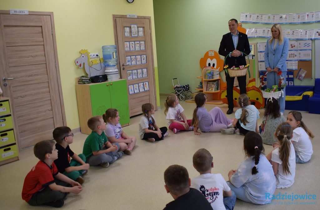 przedstawiciele gminy odwiedzają dzieci w przedszkolu. Dzieci siedzą w kręgu i uczestniczą w spotkaniu połączonym z wręczaniem upominków.