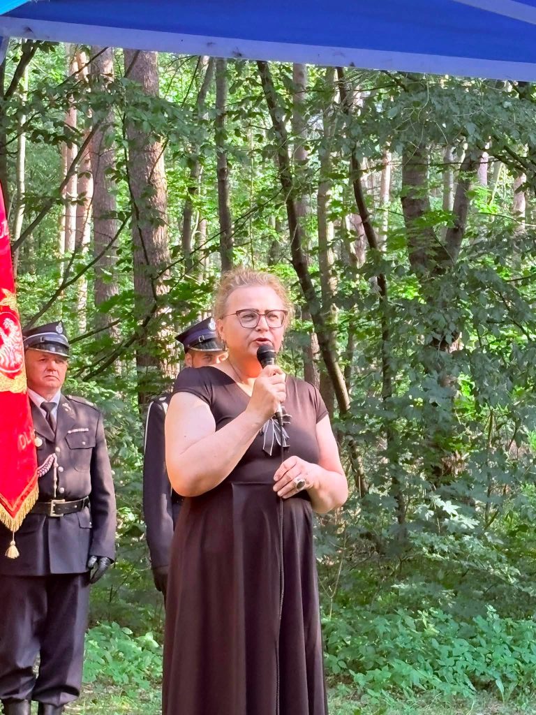 Aleksandra Biniszewska przemawia do uczestników uroczystości przy pomniku żołnierzy Armii Krajowej. W tle widoczny jest strażak.