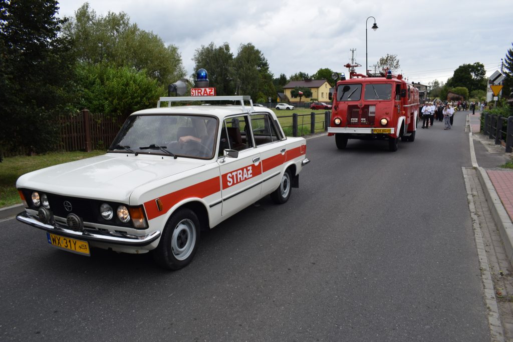Przejazd kolumny pojazdów strażackich podczas Święta Chleba. Na pierwszym planie znajduje się zabytkowy samochód strażacki, a za nim czerwony wóz strażacki.