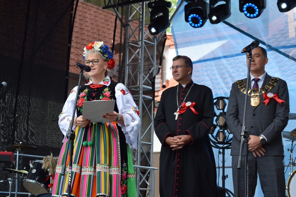 Prowadząca uroczystość oraz duchowny i przedstawiciel władz gminy na scenie podczas Święta Chleba w Radziejowicach.