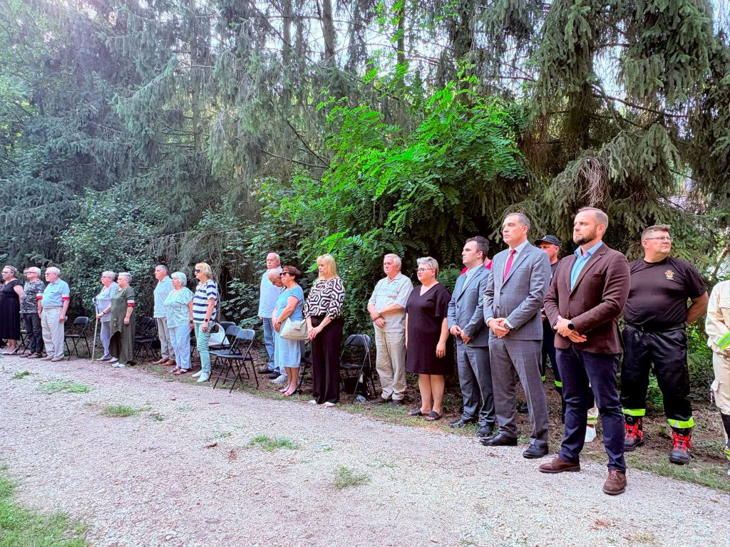 Uczestnicy uroczystości stoją w skupieniu podczas obchodów upamiętniających żołnierzy Armii Krajowej. Wśród nich są przedstawiciele władz samorządowych, strażacy i mieszkańcy.
