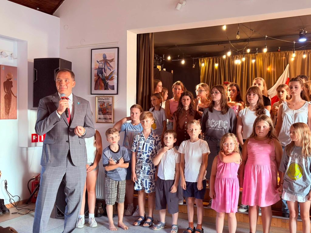 Wójt Gminy Radziejowice przemawia do uczestników po zakończeniu części artystycznej. Za nim na scenie stoją dzieci biorące udział w przedstawieniu.