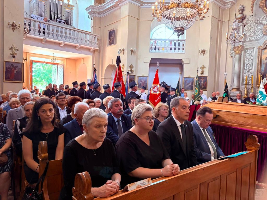 Uczestnicy uroczystości pogrzebowych siedzą w ławkach kościoła. W tle widoczna jest trumna śp. Kazimierza Drążkiewicza oraz poczty sztandarowe zgromadzone wokół niej.