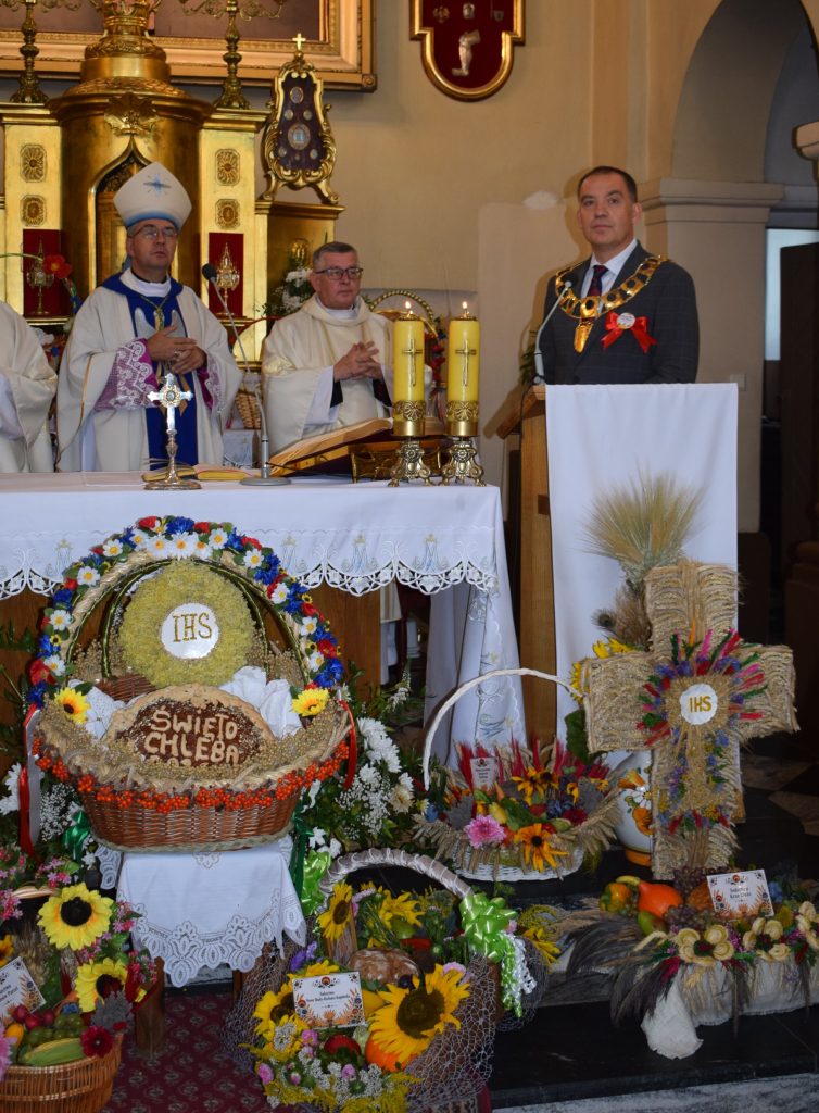 Msza święta podczas Święta Chleba w Radziejowicach. Przy ołtarzu stoją duchowni oraz przedstawiciel władz gminy, a przed nimi znajdują się wieńce dożynkowe, kosze z chlebem i kompozycje z kwiatów oraz zbóż.