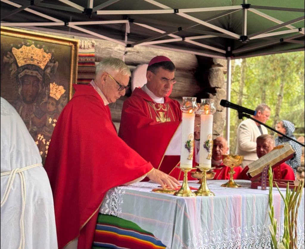 Duchowni odprawiają Mszę świętą przy ołtarzu polowym. Na stole ołtarzowym znajdują się świece, kielich i księga liturgiczna.