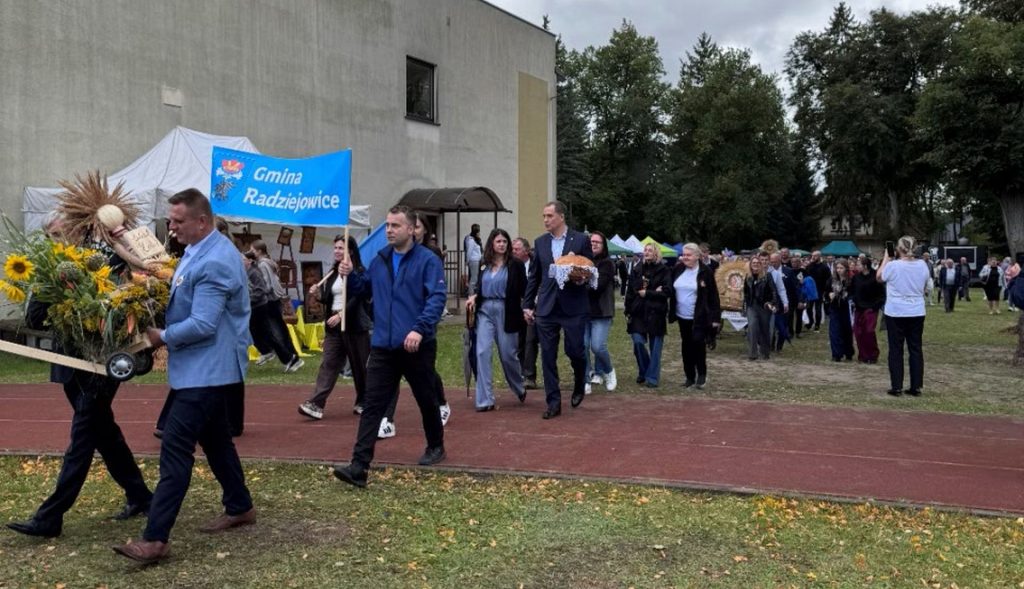 Korowód dożynkowy z przedstawicielami Gminy Radziejowice i uczestnikami wydarzenia przechodzący przez teren imprezy.