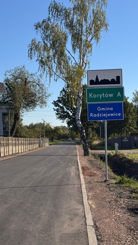 Nowa nawierzchnia drogi w miejscowości Korytów A. Przy drodze znajduje się znak z nazwą miejscowości oraz informacją o Gminie Radziejowice.