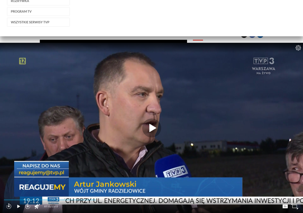 Zrzut ekranu przedstawiający kadr z programu telewizyjnego „Reagujemy” emitowanego na antenie TVP3 Warszawa. Na pierwszym planie widoczny jest Artur Jankowski, Wójt Gminy Radziejowice, udzielający wypowiedzi dziennikarzowi. W dolnej części ekranu znajduje się pasek z imieniem, nazwiskiem i funkcją rozmówcy oraz tytułem programu. W tle widoczne są inne osoby uczestniczące w nagraniu.