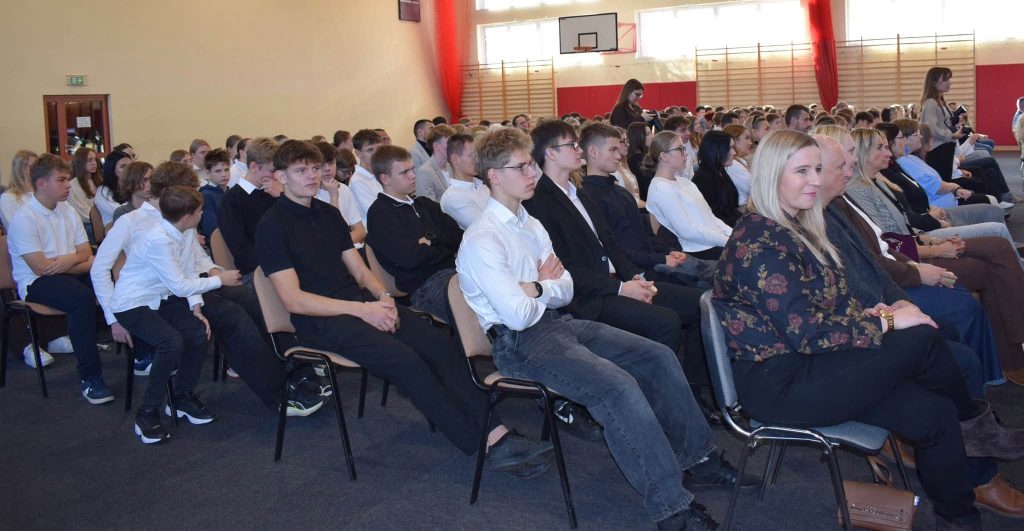 Widok publiczności zgromadzonej na Gali Sportu Powiatu Żyrardowskiego. W rzędach siedzi młodzież w eleganckich i codziennych strojach oraz dorośli uczestnicy wydarzenia. Sala gimnastyczna jest oświetlona światłem wpadającym przez wysokie okna.
