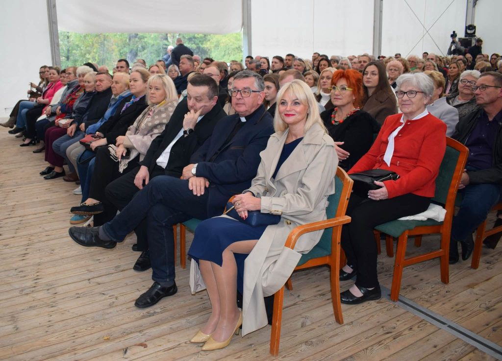Publiczność zgromadzona na koncercie zespołu „Mazowsze”. W pierwszym rzędzie siedzą zaproszeni goście, wśród nich duchowni i przedstawiciele lokalnej społeczności.