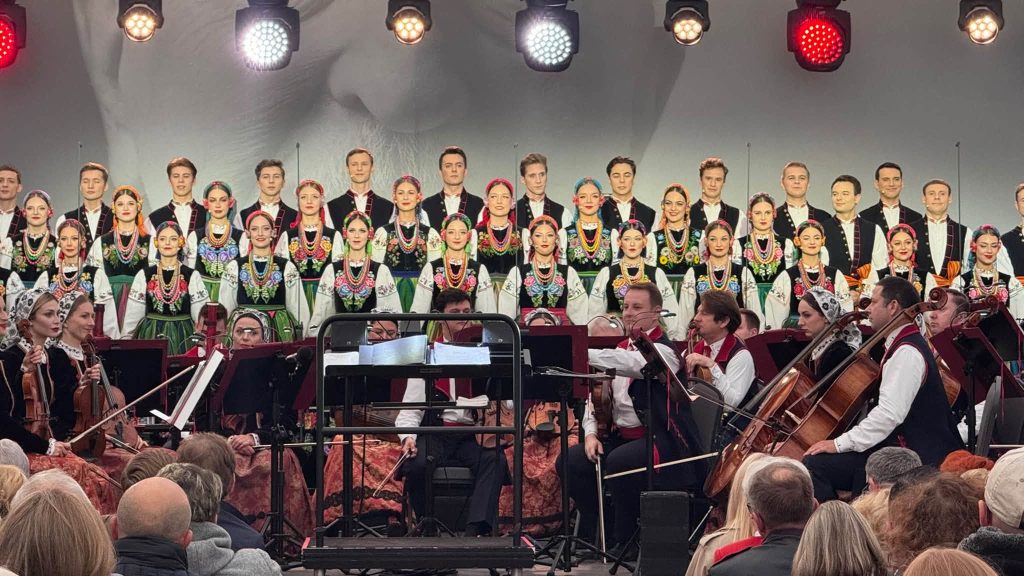 Chór i orkiestra zespołu „Mazowsze” podczas koncertu. Artyści występują w tradycyjnych strojach ludowych przed zgromadzoną publicznością.