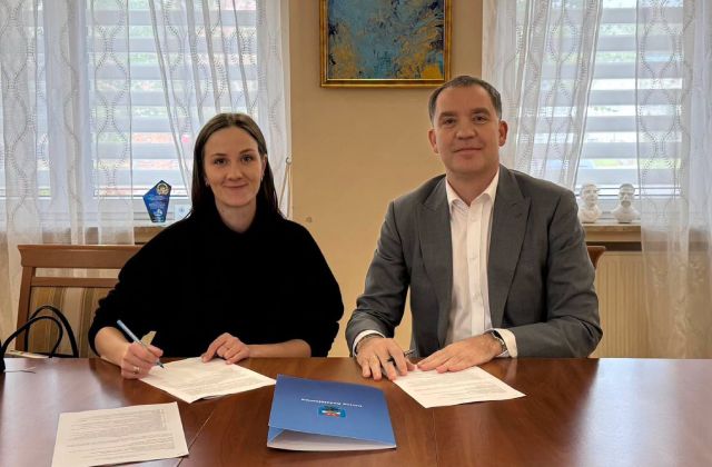 kobieta i mężczyzna siedzą przy stole na wprost kamery, przed sobą mają dokumenty które podpisują